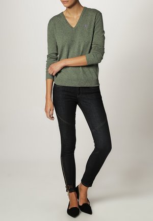 Zelený svetr s véčkovým výstřihem a žebrovanými manžetami, nošený s tmavými skinny džínami s prošíváním a zipy na kotnících; doplněný černými balerínami.