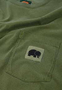 Olive green t-shirt with a chest pocket. Pocket features a black elephant graphic on a light green fabric. Soft, casual texture.