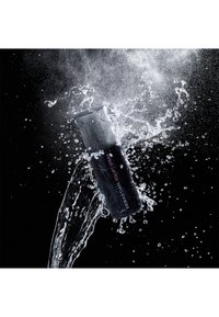 Schwarze Sprühflasche mit strukturiertem Oberfläche und runden Kappe, umgeben von spritzendem Wasser vor einem dunklen Hintergrund.