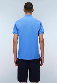 Chemise polo bleu à manches courtes en tissu lisse, avec un col standard, une fente au dos et un ourlet droit, associée à un short sombre.