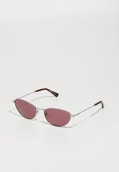 Gafas de sol en forma ovalada con lentes de color rosa oscuro y delgados marcos de metal plateado. Patillas de color negro y con patrón de carey. Diseño minimalista.