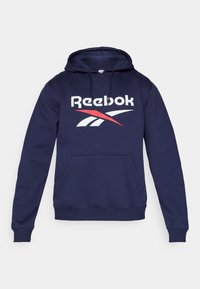 Hanorac bleumarin din țesătură moale, prevăzut cu un buzunar frontal, glugă cu șnur și un logo mare Reebok în alb și roșu.