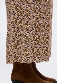 Καφέ καστόρινες μποτάκια αστραγάλου σε συνδυασμό με μια μακριά φούστα που έχει ζικ-ζακ σχέδιο σε καφέ, μαύρους και ροζ τόνους.