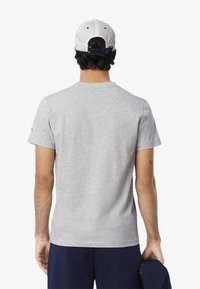 Camiseta de algodón gris con cuello redondo y mangas cortas, con una textura suave. Lleva puesto un pantalón corto azul marino y una gorra blanca en la cabeza.