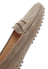 Beige suède mocassin met een textuurontwerp, decoratieve kwast en rubberen studs op de zool. Vloer is glad met perforaties voor ademend vermogen.