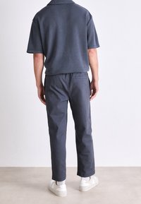 Ciemnoszara koszulka polo z krótkim rękawem w zestawie z pasującymi ciemnoszarymi spodniami. Tkanina wydaje się miękka, a fason jest luźny. Białe trampki dopełniają stylizację.