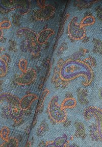 Wzorzysta tkanina z wzorem paisley w odcieniach purpury, zieleni i pomarańczu na teksturowanym niebieskim tle. Żmudne detale i żywe kolory.