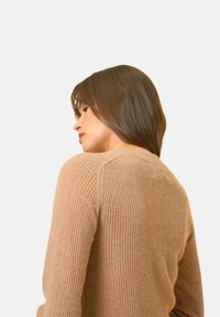 Warmer beigefarbener gerippter Pullover mit langen Ärmeln und Rundhalsausschnitt, versehen mit einer strukturierten Oberfläche und dezenten Nähdetails.