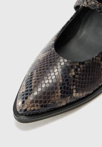 Sko med spiss tå i et svart og brunt snakeskin-mønster, teksturert skinnoppe og flat såle. Har en stropp over vristen.