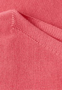 Gros plan sur un tissu tricoté rose plié montrant les détails des points et la texture.