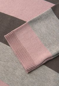 Manche de pull en tricot présentant des rayures géométriques dans des teintes de rose, gris et marron. La texture côtelée au niveau du poignet apporte un détail supplémentaire.