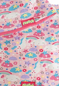 Tela de color rosa claro con patrones repetidos de unicornios, estrellas, nubes y arcoíris, con una etiqueta de marca roja en la esquina inferior izquierda.