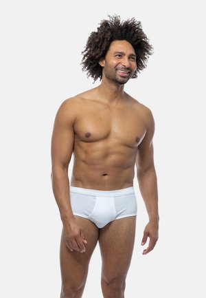 Slip di cotone bianchi con un design semplice e cintura elasticizzata, indossati da un uomo con un fisico in forma su uno sfondo neutro.
