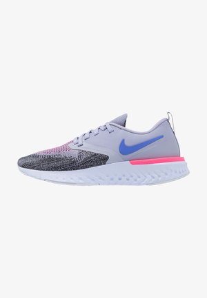 Grijze en zwarte Nike hardloopschoen met blauwe swoosh, roze accent nabij de hiel, witte gestructureerde zool en een bovenwerk van gebreide stof.