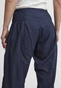 Pantalones azul marino con detalle de cintura fruncida. Hechos de una tela ligera, con un corte holgado y costuras limpias.