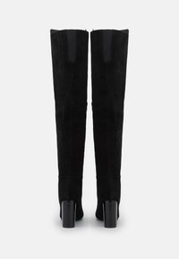 Černé semišové kozačky ke kolenům s blokovými podpatky, zadním zipem a elastickými panely na horní části lýtek pro těsné padnutí.