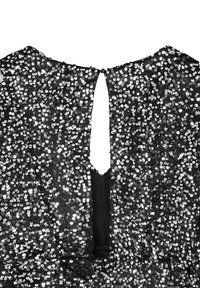Vestito nero in paillettes con design a forma di chiave sulla schiena. Il tessuto è decorato con paillettes tonde e brillanti, creando una superficie testurizzata e riflettente.