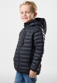 Sort dunjakke med lynlås og hætte. Har et vandret quiltet mønster og en struktureret overflade. Bærtes over denimjeans.