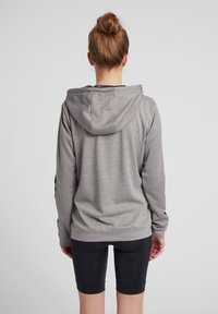 Graue Kapuzenjacke aus strukturiertem Stoff, mit langen Ärmeln und lockerer Passform, kombiniert mit schwarzen Leggings. Keine sichtbaren Logos oder Designs.