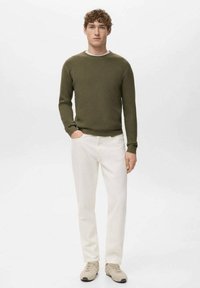 Olivgrüner, gerippter Pullover mit weißem Rundhalsausschnitt, kombiniert mit hellbeigen Hosen und beigen Sneakers. Schlichtes Design ohne sichtbare Muster oder Akzente.