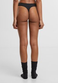 Svart truse med truseformet design og elastisk stoff, sett bakfra, som fremhever en minimal dekning og jevn tekstur.