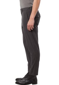 Grå byxor med smal passform, slät textur och lätt avsmalning vid ankeln, kombinerade med svarta snörstövlar.