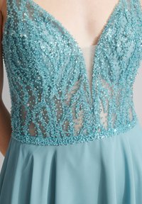 Jasnoniebieska sukienka z koralikowym, przezroczystym korpusem o skomplikowanych wzorach i głębokim dekoltem w kształcie litery V; zwiewna spódnica w jednolitym, pasującym odcieniu.