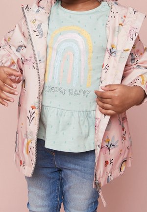 Lyserød vandtæt jakke med farverigt blomster- og dyreprint, båret over en mintgrøn top med et regnbuedesign og teksten "Choose Happy".