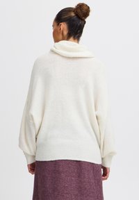 Pull en crème oversized avec col cheminée, ourlet côtelé et manches longues et larges. Matière en tricot douce et texturée.