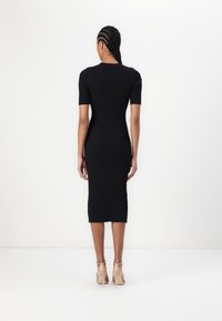 Svart ribbad midiklänning med korta ärmar, figurnära silhuett och subtil textur. Stylar med genomskinliga klacksandaler.