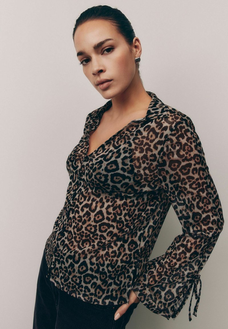 Prozračna bluza s leopard printom, s kopčanjem sprijeda, ovratnikom i lepršavim rukavima koji imaju vezice na manžetama. Smeđi i crni uzorak.