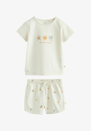 Kremfarvet babyoutfit med kortærmet skjorte med motiv af sol, skildpadde, palmetræ og teksten "min første ferie", kombineret med matchende trykte shorts.