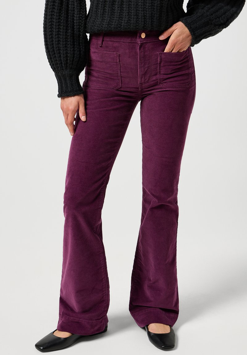 Lilla kordfløyels flared jeans med frontlommer, en tettsittende midje og en teksturert overflate, parret med svarte flate sko.