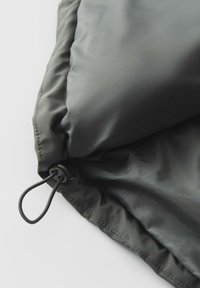 Tessuto grigio, liscio e con una texture leggermente lucida. Presenta una chiusura con cordino, bordi cuciti e una forma cilindrica.