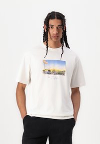 T-shirt en coton blanc avec une illustration colorée de voitures et d'une station de lavage de voitures, accompagnée du texte "Van Nuys Blvd. à Burbank" en dessous.
