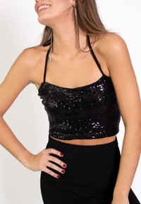 Top corto negro con lentejuelas y tirantes finos negros. Presenta una textura brillante y un escote recto. Combinado con pantalones negros de tiro alto.