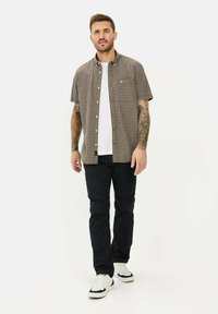 Kurzarm-Hemd mit Karomuster in Schwarz und Braun, kombiniert mit einem weißen T-Shirt, dunklen Hosen und weißen Sneakers. Lässiger Schnitt.