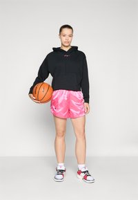 Svart cropped hettegenser med lomme foran, blanke rosa shorts, basketball i hånden, hvite sokker og flerfargede joggesko.