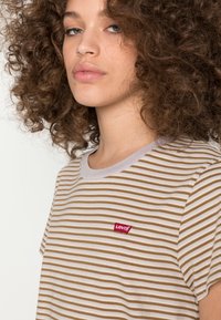 T-shirt listrado em bege e branco com mangas curtas, apresentando um decote redondo e um pequeno logo vermelho da Levi's no peito.