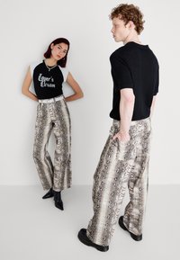 Pantaloni larghi con una stampa a serpente, caratterizzati da una palette di colori neutri. Viene indossata una maglietta nera aderente con dettagli bianchi.