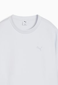 Camiseta de algodón blanca con cuello redondo y mangas cortas. Presenta un sutil logo bordado en el lado izquierdo del pecho. Textura suave y lisa.