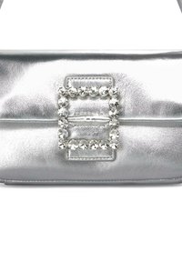 Bolso de mano de cuero plateado que presenta un cierre rectangular adornado con strass, textura suave y un diseño estructurado y elegante.