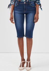 Shorts bermuda en denim bleu foncé avec un design ajust�é, taille mi-haute, et ourlet arrivant juste au-dessus du genou. Surpiqûres en cuivre.