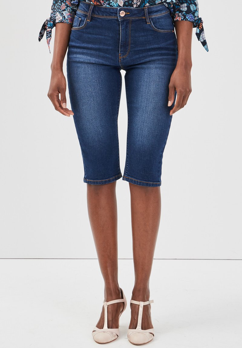 Shorts bermuda en denim bleu foncé avec un design ajusté, taille mi-haute, et ourlet arrivant juste au-dessus du genou. Surpiqûres en cuivre.