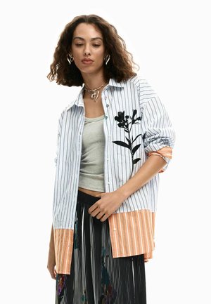 Nööbitav triibuline särk, millel on musta lillemustriga disain, oranž ääreliist ja allpool hall top. Must volditud seelik.