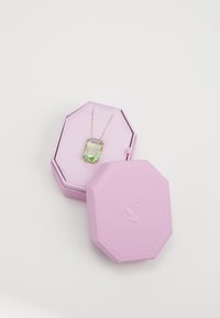 Gullkjede med en stor rektangulær grønn edelsten, plassert inne i en lys rosa åttetakket smykkeboks med teksturert overflate.