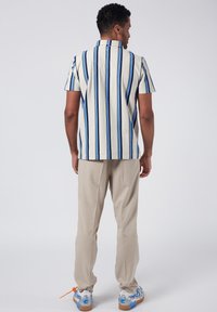 Camicetta a maniche corte a righe verticali crema e blu, abbinata a pantaloni beige chiaro. Presenta un colletto standard e una vestibilità rilassata.