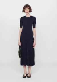 Abito a coste blu navy con maniche corte, corpetto aderente e gonna svasata alla caviglia. Abbinato a una borsa nera e scarpe basse.