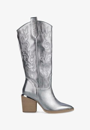 Srebrna metaliczna kowbojska botka z misternym haftem, spiczastym noskiem i warstwowym drewnianym obcasem. Gładka tekstura z dekoracyjnymi akcentami.