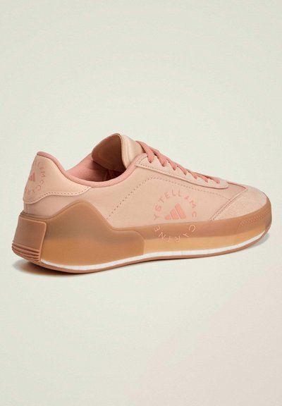 Light pink athletic shoe with a smooth synthetic upper, suede accents, rounded toe, and a translucent rubber sole. Features branded logo details.